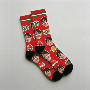 Calcetines de Navidad personalizados con la cara de un niño repetida sobre fondo rojo, con lettering Feliz Navidad, bolas de árbol y gorros de Papá Noel