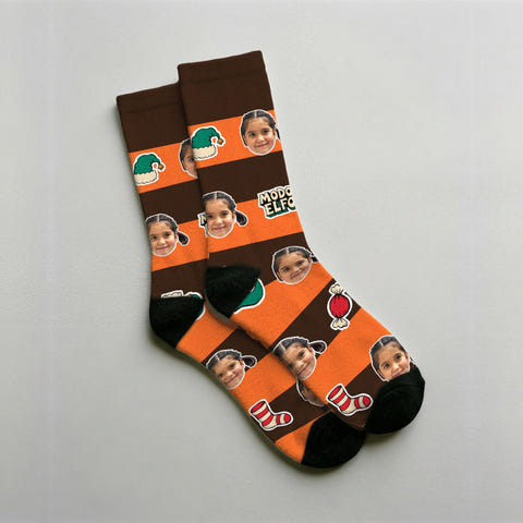 Calcetines de elfo personalizados en chocolate con la cara de un niño repetida entre gorros de elfo y cascabeles